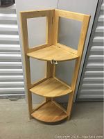 Folded wooden corner display shelf showing three triangular shelves and an open frame with cutouts.