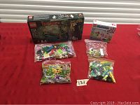 LEGO sets displayed including the unsealed Ninjago box with loose bricks, small sealed Friends polybag, and three bags of assorted bricks on a red surface.