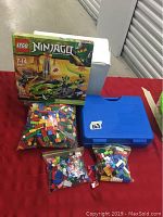Overview of LEGO Ninjago 9447 box, ziplock bags with LEGO bricks, and blue carrying case on red table