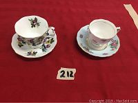 Two bone china tea cups and saucers on red fabric, one Royal Albert cup with floral pattern and one pink Colclough cup.