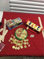 Photo showing toys on red surface including Melissa & Doug fire truck, pizza set with slice pieces and toppings, and wooden hammer bench toy.