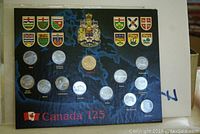 Blue chipboard display with 12 circulated provincial quarters and a one dollar coin, showing Canada 125 commemorative theme with provincial shields and coat of arms.