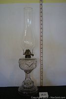 Full view of the antique oil lamp standing over 19 inches tall with clear glass chimney and bull's eye patterned base.