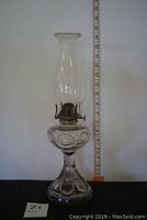 Full view of the oil lamp measuring approx. 16 inches tall with clear chimney and purple hue on glass body.