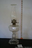 Full view of the nearly 17-inch tall antique oil lamp with glass body and chimney against a ruler for scale.