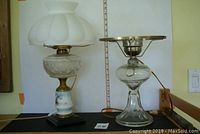 Pair of antique oil lamps converted to electric. Left lamp has a hand-painted floral pressed glass oil chamber with white glass shade. Right lamp is all clear glass with tri-lamp feature and metal top fixture.