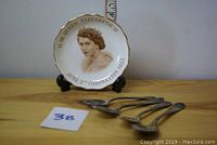 Photo of the collector plate depicting Queen Elizabeth II and four silver spoons on display.