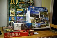 Photo showing multiple puzzle boxes stacked, including a 10 deluxe puzzle box, a deluxe 10 puzzle pack, Puzzle Collection 750 piece box, and Springbok 1000 piece box.