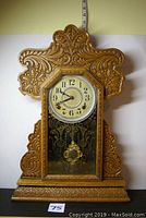 Front view of restored antique pendulum clock showing ornate carved wooden case, round dial with Arabic numerals, painted glass lower door panel, and pendulum behind glass.