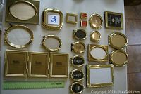 Collection of 17 brass picture frames arranged and photographed together on white surface including various shapes and sizes.