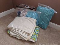 Folded sheets, pillowcases, and vacuum sealed blue and patterned fabric bundles on floor by corner