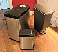 Overview of three trash cans: double stainless steel unit, medium plastic wheeled bin, small stainless steel can.