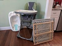 Full view of the Graco high chair, plastic baby bath, and two beige mesh safety gates arranged together