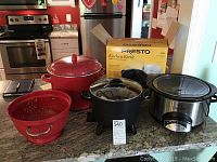 Overview of all items: Rival Crock-Pot slow cooker, Presto Kitchen Kettle fryer in box, large red enamel pot with lid, and matching colander.