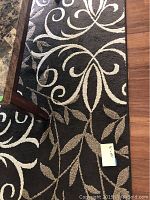 Close-up of the rug showing floral and leaf pattern in beige on a brown background.