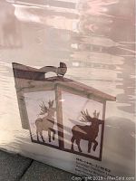 Close-up image of a Grandrich stencil outdoor lantern featuring a weathered bronze finish metal frame with moose stencil design on clear panels.