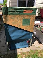 Folded Coleman cot with dark green fabric cover, displaying Coleman logo and nature pattern