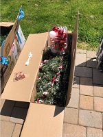 Open box showing artificial snow needle pine tree and loose Christmas balls in clear plastic container.