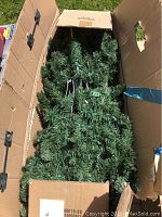 Artificial Christmas tree branches inside a large cardboard box, showing dense green needles.
