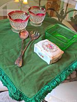 Front angle showing two ruby red rimmed glass candle holders, green glass dish, porcelain box with floral design, and sterling servers