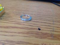 Silver engagement ring with clear stones shown on wooden surface.