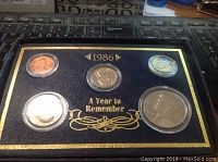 Photo of first 1986 coin collection set with five coins in protective casing on blue fabric with gold trim and text.