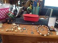Photo of assorted costume jewelry spread across a wooden desk, showing necklaces, bracelets, brooches, rings, and earrings with various colors and metal finishes.