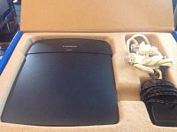 Top view of the Linksys N300 router inside packaging with included cables beside it.