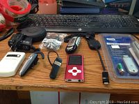 Photo showing Eclipse M3 P MP3 player, wireless earphones, Bluetooth earpiece, USB cables, and small electronic accessories on a desk in front of a keyboard.