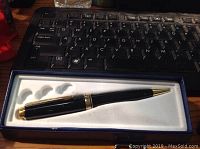 Black and gold-trimmed pen in box shown on a desk with keyboard background