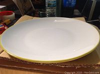 Top view of a dinner plate showing white surface and thin yellow rim against cardboard background.
