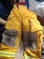 Yellow firefighter rescue pants with red suspenders laid out showing front with multiple pockets, reinforced knees, and yellow reflective strips on hems.