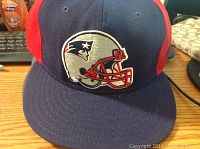 Front view of New England Patriots football helmet logo hat in navy and red colors.
