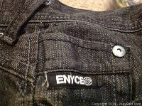 Close-up of black Enyce jeans label and fabric texture with metal rivet.