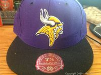 Purple and black Minnesota Vikings cap with Viking head logo embroidered on front, red Mitchell & Ness tag on brim, size 7 5/8