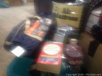 Photo of the lot showing air mattress in packaging, blue tent bag, paperback dictionary, silver electronic device, plastic jug with red liquid, and a green zippered case