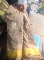 Photo of firefighter bunker gear pants laid out showing the leg with yellow reflective bands at the bottom, visible wear and dirt marks.