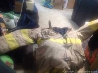 Firefighter turnout jacket with arms extended, showing reflective stripes and fabric condition.