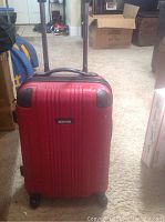 Front view of the red hard shell carry-on suitcase with telescoping handle extended and spinner wheels visible.