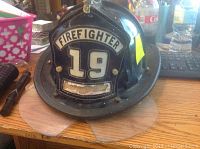 Front view of black Cairns firefighter helmet showing the firefighter badge number 19 and face shield.