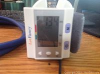 Digital wrist blood pressure monitor showing a reading of 134 mmHg on the LCD screen with buttons and cuff attached, placed on a wooden surface.