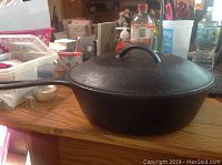 Closed view of the cast iron frying pan on wooden table with lid on top.