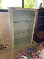 Front view of white glass display case showing glass shelves and door with latch
