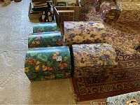 Top and side view of five colorful floral storage trunks arranged on a carpeted floor showing size variation and pattern.