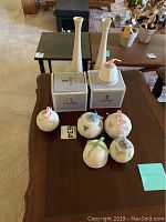 Two white Lenox bud vases standing behind three Lladro ornaments and two Lladro boxes on brown table.