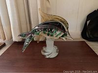 Multicolored glass fish figurine with detailed dorsal fin displayed on a wooden surface with neutral background.