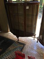 Front angled view showing full cabinet with curved glass front and wood frame, situated near a door and wall.
