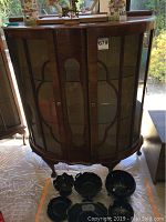 Front view of the vintage wooden curio cabinet with glass mesh doors and black ceramic bowls in front.