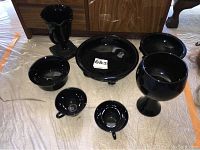 View of all seven black glassware pieces arranged on floor, highlighted the glossy finish and shapes.