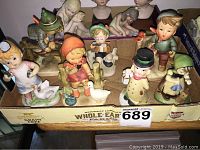 Various small figurines, numerous children characters mostly under 3 inches tall, with animals like geese, arranged inside a box.
